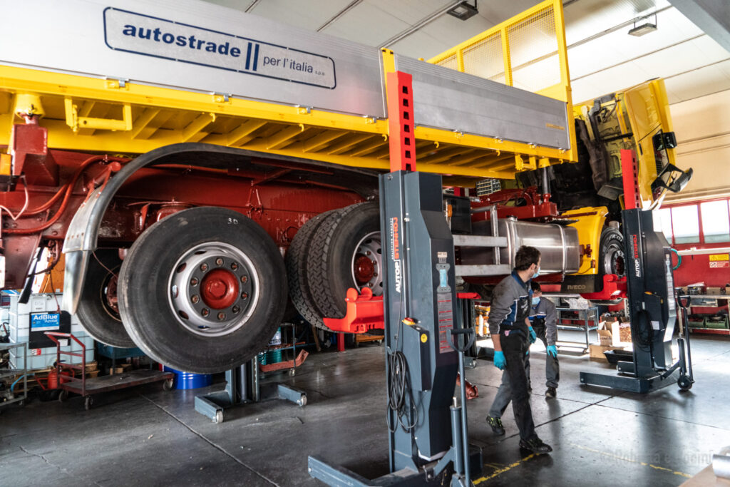 Camion sollevato in officina con meccanici al lavoro.