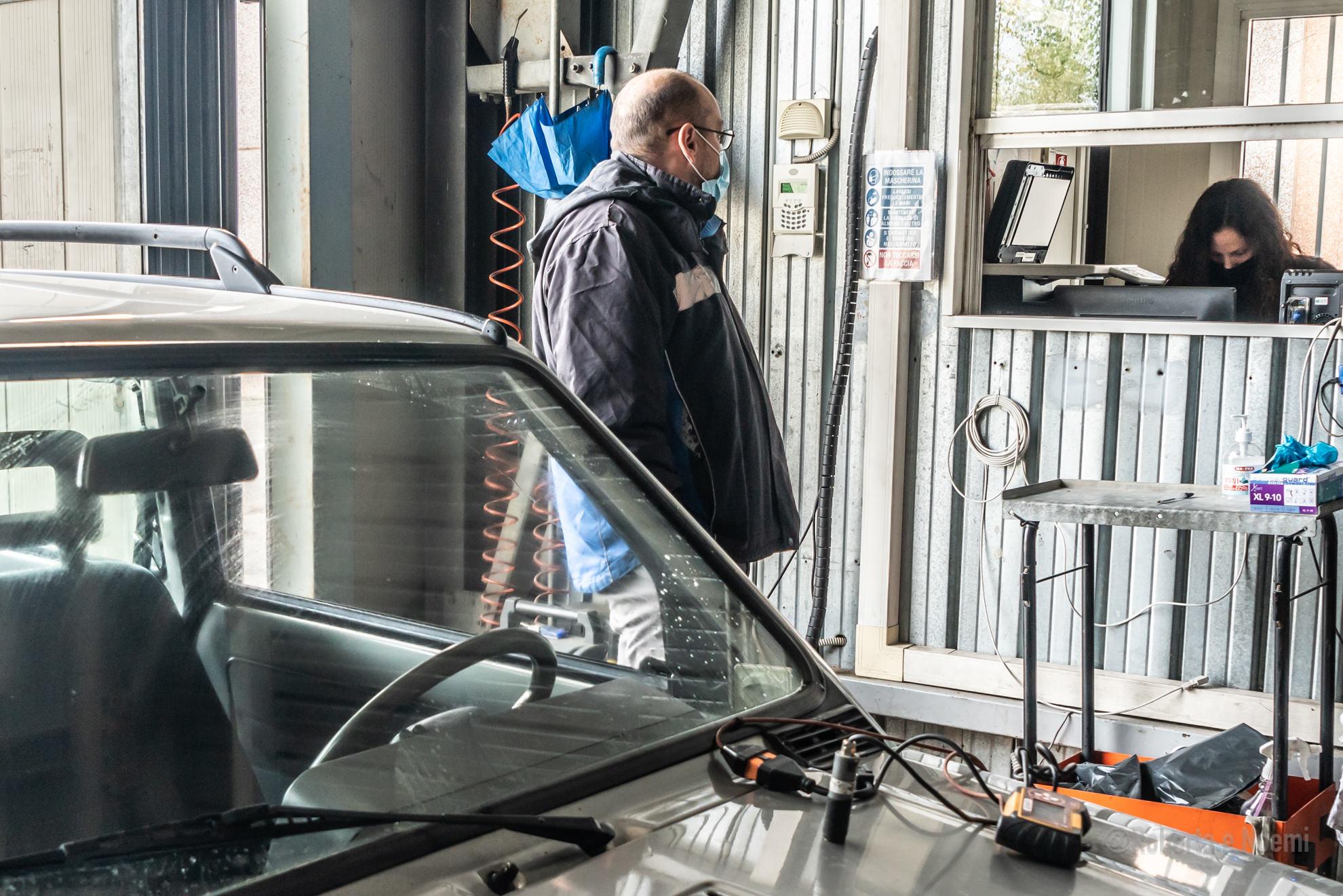 Uomo con mascherina in un'officina, vicino a un'auto.