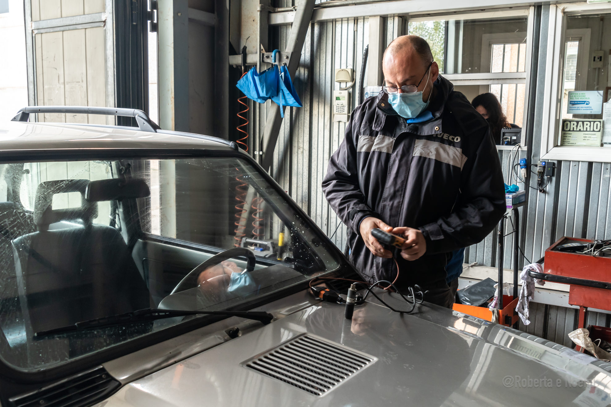 Meccanico controlla auto in officina con mascherina.